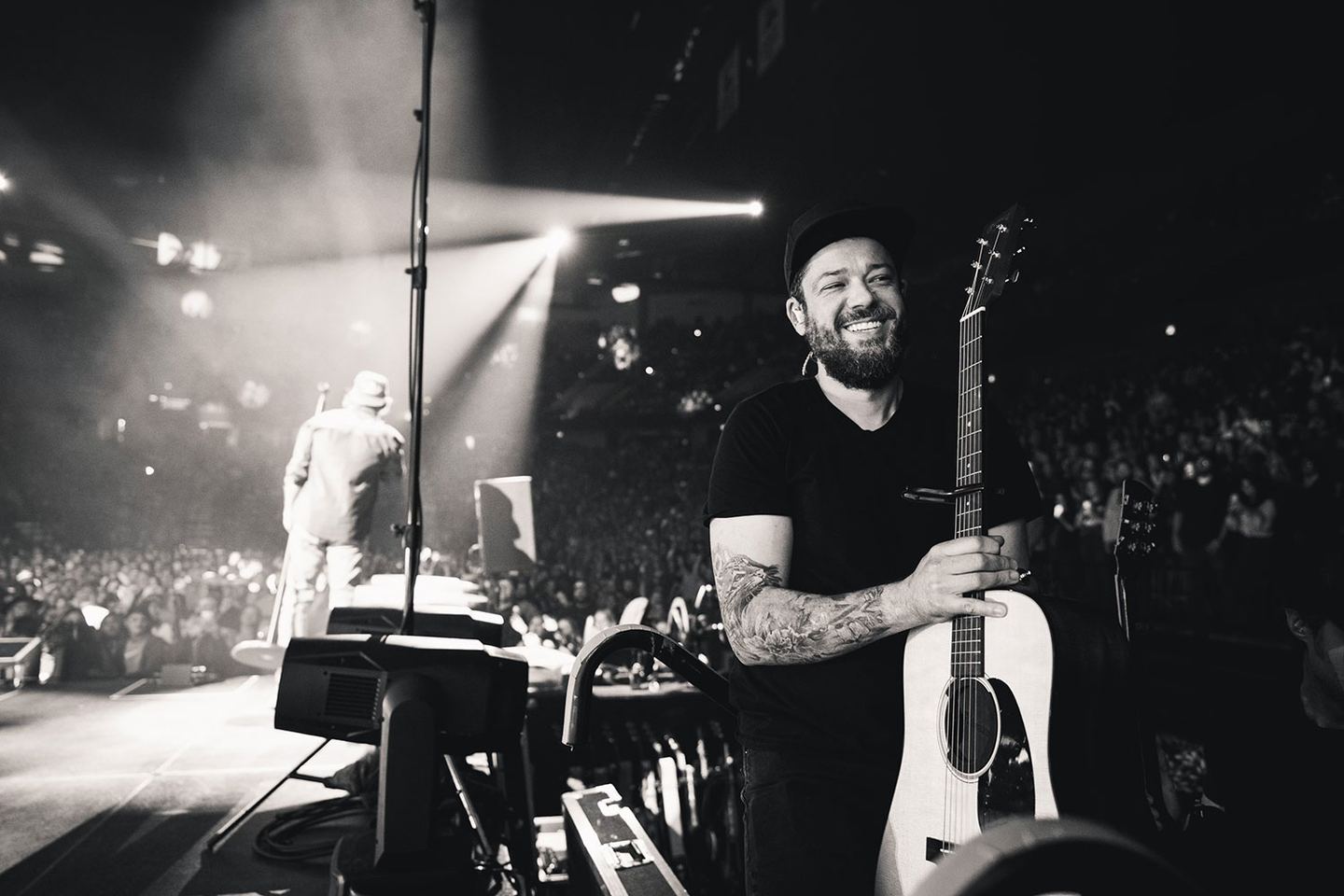 Black and white photo of a man backstage holding an acoustic guitar